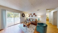 This single-floor residence offers a thoughtfully arranged layout that maximizes comfort and functionality. The living room serves as the heart of the home, featuring warm hardwood-style flooring, a textured ceiling, and a sliding glass door that opens to a private outdoor balcony with views of lush greenery. The space is defined by its nature-inspired aesthetic, highlighted by a collection of organic wood-slice wall art, a sunburst mirror, and a cohesive teal and earth-tone color palette. A leather sofa, velvet accent chair, and a solid wood coffee table complete the inviting seating area.

The bedroom is a serene retreat with a large window that draws in natural light and frames views of surrounding foliage. It features hardwood-style flooring, a textured ceiling, and a full-width sliding closet that provides generous storage. Botanical-themed framed artwork adds a calm, nature-forward character to the room.

The kitchen is equipped with light wood cabinetry, white countertops, and stainless steel appliances including a range and refrigerator, offering a clean and practical cooking space. The bathroom features warm wood vanity cabinetry, a white countertop with an integrated sink, a wide mirror, and bright overhead lighting, creating a tidy and functional space throughout.