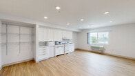 Located at 2274 Newport Blvd in Costa Mesa, California, Unit 404 is a thoughtfully designed studio space that maximizes functionality within a compact, single-floor layout. The open living area features warm light wood flooring and crisp white walls, creating a bright, clean aesthetic throughout. Recessed lighting illuminates the space evenly, complementing a window that invites natural light and provides views of the surrounding neighborhood. A wall-mounted climate control unit ensures year-round comfort.

The kitchen area is fully equipped and seamlessly integrated into the main living space. It features an all-white cabinetry arrangement with ample upper and lower storage, a white electric range with cooktop, a built-in microwave, a dishwasher, and a single-basin sink — all set against light wood flooring that ties the space together cohesively.

The bathroom is designed with accessibility in mind, featuring stainless steel grab bars positioned throughout, including near the toilet and along the walls. A full-size soaking tub with a handheld showerhead and additional grab bar support, a vanity, and smooth, easy-clean flooring complete the well-appointed space. The overall design of the unit emphasizes simplicity, practicality, and accessibility in a convenient Costa Mesa location.