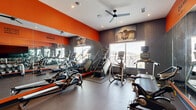 Located at 1818 Park Ave in Dallas, TX, this fitness center is a compact yet thoughtfully designed workout facility that maximizes every square foot of its single-floor layout. The space is defined by a bold, energizing color palette of vivid orange and deep charcoal gray, creating a high-energy atmosphere that encourages activity. Full-length mirrors line one wall, visually expanding the room while allowing users to monitor their form during exercise.

The cardio zone is well-stocked with a variety of machines, including treadmills, a stair climber, ellipticals, a rowing machine, and a stationary spin bike. A dedicated free weights area features a full dumbbell rack alongside a weight bench, catering to strength training needs. Motivational phrases such as "Excuses Don't Burn Calories" are stenciled prominently on the walls, reinforcing the facility's fitness-forward ethos.

Large windows allow natural light to filter in, while a ceiling fan and recessed lighting ensure the space remains comfortable during intense workouts. Yoga mats are available on wall-mounted holders near the entrance, supporting flexibility and cool-down routines. Athleically themed wall art and photography add visual interest. The polished concrete floors are durable and easy to maintain, completing this practical, purpose-built fitness environment.