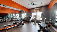 Located at 1818 Park Ave in Dallas, TX, this fitness center is a compact yet thoughtfully designed workout facility that maximizes every square foot of its single-floor layout. The space is defined by a bold, energizing color palette of vivid orange and deep charcoal gray, creating a high-energy atmosphere that encourages activity. Full-length mirrors line one wall, visually expanding the room while allowing users to monitor their form during exercise.

The cardio zone is well-stocked with a variety of machines, including treadmills, a stair climber, ellipticals, a rowing machine, and a stationary spin bike. A dedicated free weights area features a full dumbbell rack alongside a weight bench, catering to strength training needs. Motivational phrases such as "Excuses Don't Burn Calories" are stenciled prominently on the walls, reinforcing the facility's fitness-forward ethos.

Large windows allow natural light to filter in, while a ceiling fan and recessed lighting ensure the space remains comfortable during intense workouts. Yoga mats are available on wall-mounted holders near the entrance, supporting flexibility and cool-down routines. Athleically themed wall art and photography add visual interest. The polished concrete floors are durable and easy to maintain, completing this practical, purpose-built fitness environment.