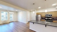 Located at 3528 W Seltice Way in Coeur d'Alene, Idaho, this single-floor unit offers a clean, modern layout with a thoughtful mix of finishes and functional design. The open-concept kitchen serves as a central feature, anchored by a generously sized island with a dark countertop, an integrated sink, and pendant lighting overhead. Light wood cabinetry lines the walls alongside a full suite of stainless steel appliances, including a refrigerator, range, and microwave. A tile backsplash adds a subtle decorative touch behind the cooking area.

Wood-style flooring extends through the kitchen and into the main living area, which benefits from natural light streaming through large windows and a glass door that opens to a private balcony with views of the surrounding building exterior. Baseboard heating is present throughout, providing consistent warmth. The carpeted bedroom offers a quieter retreat, with a window, baseboard heater, and an electrical panel recessed into the wall. The bathroom includes a white vanity countertop, vessel sink, chrome fixtures, and mirror. Additional closet storage is accessible off the main living space, contributing to the unit's overall practicality.