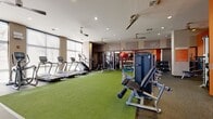 Located at 144 Moreland Ave NE in Atlanta's vibrant Inman Park district, this fitness center offers a thoughtfully designed, single-floor space that accommodates a comprehensive range of workout activities. The layout is organized to maximize functionality, with distinct zones dedicated to cardio, strength training, and open-floor exercise.

The cardio section lines the perimeter near a wall of large windows, allowing natural light to fill the space and providing outdoor views during workouts. Multiple treadmills, elliptical machines, and a stair climber are positioned here, each equipped with individual displays. Ceiling fans are distributed throughout, maintaining airflow across the entire floor.

The strength training area features a well-stocked dumbbell rack, cable machines, multi-function cable stations, and a medicine ball and kettlebell rack. Full-length mirrors along one wall visually expand the space and aid in form monitoring. A turf surface occupies the central open area, providing a functional zone for dynamic training and stretching exercises.

Bold orange accent walls energize the space visually, complemented by stone-textured wall panels that add a refined, modern aesthetic. Recessed lighting ensures consistent illumination throughout. The facility also includes two restrooms and a built-in cabinetry unit with a mounted television, rounding out a complete and practical fitness environment.
