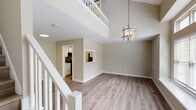 Located at 1009 Fir Pl in Greensboro, NC, this two-story home showcases a thoughtfully designed interior with a neutral color palette and light wood-look flooring carried throughout both levels. The main living area immediately impresses with its dramatic double-height ceiling, which creates an expansive, airy atmosphere. A contemporary metal chandelier serves as a central focal point, complementing the open layout below. A white-railed staircase connects the two floors, while an upper-level overlook adds architectural depth to the space.

Large windows with deep sills flood the living area with natural light and offer views of the surrounding greenery, enhancing the open feel. A pass-through window connects the living area to the kitchen, maintaining visual connectivity between spaces. The galley-style kitchen is well-appointed with white cabinetry, quartz-style countertops, and stainless steel appliances, including a range, microwave, refrigerator, and dishwasher.

The upper level features a barn door accent that adds a modern farmhouse touch, alongside an open landing overlooking the main floor. Bathrooms include a full tub-shower combination and a secondary bath with a floating wood-toned vanity and angled ceiling detail. The overall ambiance is clean, bright, and move-in ready.