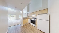 Located at 11030 Main St in Bellevue, WA, this two-story residence offers a well-designed layout spread across two evenly sized floors. The main level features light hardwood-style flooring throughout the kitchen and hallway areas. The kitchen is equipped with light maple cabinetry, granite-style countertops, a full suite of white appliances including a refrigerator, electric range, and dishwasher, along with a stainless sink and under-cabinet range hood. Soaring double-height ceilings in the main living area create an open, airy atmosphere, with track lighting adding functional illumination. A staircase with a warm wood handrail connects the two floors. The hallway on the main level provides access to a full bathroom, which features hardwood-style flooring, a maple vanity with granite-style countertop, a wall-mounted mirror with overhead lighting, and a shower-tub combination. In-unit stacked laundry is also conveniently located on this level. The upper floor is carpeted and bathed in natural light from multiple windows, offering an open loft-style space with views to the lower level. The overall aesthetic is clean, neutral, and modern, making for a bright and functional living environment.