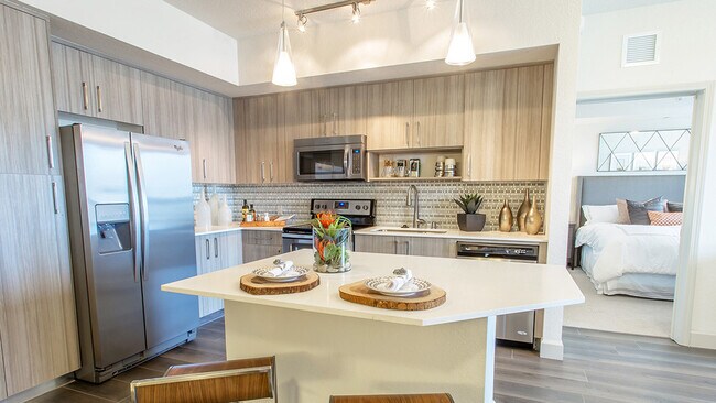 Cocina de lujo de concepto abierto en un apartamento, con isla de cuarzo, electrodomésticos de acero inoxidable y gabinetes de madera. - Griffis North Olive
