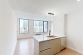 Located at 626 Summit Ave in Jersey City, NJ, this modern studio offers a thoughtfully designed open-concept layout that maximizes every inch of its compact footprint. The combined kitchen and living area is anchored by large, black-framed floor-to-ceiling windows that flood the space with natural light and frame striking panoramic views of the Jersey City skyline, including notable landmarks such as a historic church below. Light-toned hardwood flooring runs throughout, complementing the clean white walls and recessed lighting overhead.

The kitchen is a standout feature, boasting a sleek waterfall-edge island with a white quartz countertop, matte black fixtures, and an integrated sink. Flat-front cabinetry in a warm taupe finish pairs with a full suite of stainless steel appliances, including a gas range, refrigerator, and built-in microwave. A sculptural, looping pendant light adds a contemporary artistic touch above the island.

The bathroom is finished with large-format neutral tile, a wall-mounted floating vanity, an illuminated LED mirror, and matte black hardware accents, creating a clean, spa-like atmosphere. Throughout the unit, the minimalist design aesthetic, modern finishes, and expansive city views come together to create a bright, functional, and stylish urban living space.