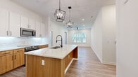 Located at 2031 Synergy Ln in Sarasota, FL, this well-appointed single-story home offers a thoughtfully designed open-concept layout with 2 bedrooms, 2 bathrooms, and three closets. Light wood-look flooring flows seamlessly throughout, complemented by crisp white walls and modern fixtures that create a clean, contemporary aesthetic.

The kitchen is a standout feature, showcasing a large quartz-topped island with an undermount sink and matte black faucet, two-tone cabinetry pairing white uppers with warm wood lowers, a matching quartz backsplash, and stainless steel appliances. Geometric pendant lanterns hang above the island, adding a stylish focal point that connects visually to the open living area beyond, which is equipped with a ceiling fan and a bright window framing views of the lush Florida greenery outside.

The spacious primary bedroom features dual windows that bathe the room in natural light, while the second bedroom also benefits from natural light through its own window. Both bedrooms are served by well-organized walk-in closets with built-in shelving and hanging rods. The bathroom includes a soaking tub, subway-tiled surround, and a white vanity with matte black accents. A dedicated laundry room houses a full-size washer and dryer alongside additional built-in shelving for extra storage.
