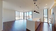 Located in the heart of downtown Tucson, this contemporary single-floor residence showcases a thoughtfully designed open-concept layout with rich hardwood flooring throughout. The expansive living and dining area is anchored by dramatic floor-to-ceiling windows and glass sliding doors that frame striking views of the Tucson skyline, flooding the space with abundant natural light. A private balcony extends the living space outdoors, offering direct access to the surrounding cityscape.

The kitchen is a standout feature, centered around a large island clad in bold geometric patterned tile and topped with a clean white quartz countertop. Warm natural wood cabinetry, subway tile backsplash, stainless steel appliances—including a gas range and French door refrigerator—and a cluster of modern pendant lights complete the well-appointed space. In-unit stacked laundry is conveniently integrated into the open living area.

The bedrooms offer generous proportions with floor-to-ceiling windows providing city views and ample natural light. The bathroom features striking geometric patterned floor tile, a sleek dark vanity with white countertop, a walk-in glass shower, and a pendant light fixture. A spacious walk-in closet with multi-level shelving provides substantial storage.