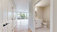 Located at 27S Main St in Attleboro, Massachusetts, this thoughtfully designed unit offers a well-organized single-floor layout that maximizes every square foot. The open-concept living and kitchen area is anchored by a wall of large, black-framed windows that flood the space with natural light and offer pleasant outdoor views of surrounding greenery. Light-toned hardwood-style flooring runs throughout, enhancing the bright and airy ambiance.

The kitchen is outfitted with white shaker-style cabinetry featuring black hardware, a white subway tile backsplash, and a full suite of stainless steel appliances including a refrigerator with ice maker, a range, and a dishwasher. A wall-mounted mini-split unit provides efficient climate control.

A hallway leads to three closets, offering generous storage options rarely found in compact units. The full bathroom is finished with tasteful attention to detail, showcasing a white shaker vanity with a quartz countertop, a round black-framed mirror, hexagonal mosaic tile flooring, and warm neutral wall tones. Clean white trim and doors are consistent throughout, lending the unit a cohesive, modern aesthetic. The overall design balances contemporary finishes with functional, practical living.