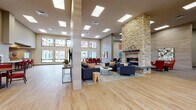 Located at 17309 40th Avenue NE in Arlington, Washington, this single-floor community facility offers a thoughtfully designed layout with a variety of functional and social spaces. The grand entrance lobby features soaring double-height ceilings, large clerestory windows, polished large-format tile flooring, and a built-in reception counter, creating an impressive and welcoming first impression. Adjacent to the lobby, an expansive open lounge area showcases light hardwood flooring, generous skylights, and a dramatic floor-to-ceiling stacked-stone fireplace that serves as a central focal point. This area transitions into a casual dining nook with a wood table, red upholstered chairs, and tall windows offering views of the surrounding residential courtyard. A full kitchen with dark cabinetry, a gas range, white countertops, and a breakfast bar with red barstools supports catering and community dining needs. Additional lounge areas feature plush seating, wall-mounted televisions, and curated artwork throughout. A carpeted game room includes a pool table and accent seating, while a quieter sitting alcove offers comfortable yellow lounge chairs and framed artwork, ideal for relaxed retreat. Natural light permeates the entire space through skylights and large windows, contributing to a bright, welcoming community atmosphere throughout.