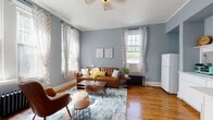 Located at 508 N Tryon Street in the heart of uptown Charlotte, North Carolina, this single-floor space combines classic architectural character with thoughtful modern updates. Throughout the unit, rich hardwood floors provide a warm foundation that complements the cool, calming blue-grey walls and crisp white trim and baseboards. The living area is generously proportioned with impressively tall ceilings and large, floor-to-ceiling windows adorned with patterned curtains that flood the room with natural light. A classic cast-iron radiator adds a distinctive vintage touch, while crown molding reinforces the space's historic charm. The kitchen is clean and functional, featuring white shaker-style cabinetry, light countertops, subway tile backsplash, and an open display shelf — all carried out in a cohesive, bright aesthetic that mirrors the overall palette of the home. An additional room offers flexible use as a bedroom or flex space, featuring the same tall ceilings, hardwood floors, and a classic paneled white door. The unit's consistent design language — characterized by its soft blue-grey walls, warm wood floors, generous ceiling heights, and ample natural light — creates a cohesive and inviting atmosphere throughout.