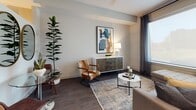 This thoughtfully designed single-floor space offers a seamless blend of modern aesthetics and functional living. The kitchen is outfitted with stainless steel appliances, two-toned cabinetry featuring white upper cabinets and grey lower cabinets, white subway tile backsplash, open shelving, and a large window that draws in natural light — creating a bright and efficient workspace for cooking and entertaining. The living area is warm and inviting, featuring dark hardwood-style flooring, neutral walls, and ample space for seating and décor. A trio of oval gold-framed mirrors adds a distinctive design element, complemented by a glass-top bistro table and leather accent chairs that lend a mid-century modern character. The bedroom is elegantly appointed with a curated gallery wall, warm lighting from bedside lamps, and a soft, neutral color palette that promotes a restful atmosphere. The bathroom features large-format marble-style floor tiles, a grey vanity with a white countertop, and modern light fixtures, offering a clean and polished finish. Throughout the space, dark hardwood-style flooring provides continuity, while the overall design balances contemporary style with comfortable, livable details.