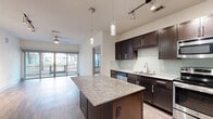 This 2-bedroom, 2-bathroom residence is thoughtfully designed across a single floor, offering a comfortable and functional layout with modern finishes throughout. The open-concept kitchen and living area serves as the heart of the home, featuring rich dark-espresso cabinetry, granite countertops, a subway tile backsplash, and a full suite of stainless steel appliances including a refrigerator, range, microwave, and dishwasher. A granite-topped kitchen island provides additional prep space and casual seating. Pendant and track lighting illuminate the kitchen, while the living area benefits from wood-look flooring and a ceiling fan. Sliding glass doors open directly to a private balcony, flooding the space with natural light and offering outdoor views. The primary bedroom is generously sized with plush carpet flooring and connects to a well-appointed en-suite bathroom featuring dark vanity cabinetry, granite countertops, large-format tile flooring, and access to a walk-in closet with built-in shelving and hanging rods. The second bedroom is equally comfortable, also carpeted, with easy access to the second full bathroom. Additional conveniences include multiple closets for ample storage, a dedicated laundry area, and a utility room.