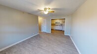 This single-floor residence offers a practical and comfortable layout designed for everyday living. The living area is bright and open, featuring light-toned hardwood-style flooring, neutral gray walls, a textured ceiling, and a ceiling fan with integrated lighting. A louvered closet door adds a functional touch, while a window allows natural light to filter in. The space flows directly into the kitchen, which is thoughtfully arranged in an L-shaped configuration. White cabinetry lines the walls from floor to ceiling, providing generous storage, while gray laminate countertops offer ample workspace. The kitchen is equipped with a white electric range, dishwasher, refrigerator, and a double-basin sink. An electrical panel is conveniently located adjacent to the kitchen. The bedroom is carpeted in a neutral blue-gray tone and includes a window fitted with blinds for natural light and privacy. The bathroom features light hardwood-style tile flooring, a full tub-shower combination with a white surround, a toilet, and a vanity with a speckled countertop. Throughout the space, consistent neutral tones and clean finishes create a cohesive and move-in-ready environment.