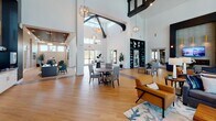 This single-story clubhouse is designed as a sophisticated community amenity space, combining functionality with upscale contemporary aesthetics. The grand entrance lobby sets the tone immediately, featuring soaring double-height ceilings, large-format hexagonal tile flooring, a decorative copper-toned ceiling inset, and a formal reception desk framed by textured wall paneling and curated artwork.

The main lounge area showcases warm wood-look tile flooring, a sleek linear fireplace set against a geometric tile accent wall, and a gold-toned chandelier. Floor-to-ceiling glass doors connect the interior directly to an outdoor terrace, allowing abundant natural light and views of the surrounding landscaping and pool area.

Adjacent to the lounge, the game and entertainment room features a billiards table, dark accent walls, large windows, and a central kitchen island with quartz countertops and pendant lighting. The catering kitchen nearby is fully equipped with stainless steel appliances, ample cabinetry, and a utility sink.

A dedicated conference room offers a wood conference table, modern pendant lighting, and a wall-mounted display. A cyber café nook with individual seating areas and natural window views completes this well-appointed amenity space.