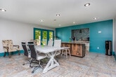 Located at 3797 Lavista Rd in Tucker, GA, this distinctive single-floor space makes a bold design statement through its signature teal color palette, carried consistently throughout every area. The main gathering hall impresses with soaring vaulted ceilings finished in dark-stained wood beams, rich dark herringbone hardwood flooring, and corrugated metal wainscoting panels that add an industrial-chic character. A pool table anchors the open recreation area, while large windows and teal-trimmed French doors flood the space with natural light and provide outdoor access.

A mezzanine level overlooks the main floor, offering a dedicated workspace with built-in shelving, workstations, and additional seating — connected by a sleek metal-railed staircase. A lounge area on the upper level features a tufted velvet sofa and accent wall sconces, creating an intimate retreat above the activity below.

The kitchen is well-appointed with white cabinetry, granite countertops, a gas range, and a striking teal herringbone tile backsplash. A separate wet bar area mirrors this aesthetic with its own sink, white cabinetry, and matching tile backsplash. A secondary lounge area provides comfortable seating, a large wall-mounted television, and direct access to an outdoor deck, completing this dynamic and thoughtfully designed space.