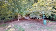 This single-floor space offers a thoughtful blend of comfortable interior living and dedicated outdoor amenity. The dog park is a standout feature, enveloped by mature, leafy trees that provide generous shade throughout the day. A classic metal bench is nestled among the trees on a mulched ground surface, creating a tranquil retreat for pet owners. A perimeter fence ensures a secure environment for pets to roam freely.

Inside, the interior rooms are finished with warm, neutral tones and plush carpeting, lending a clean and inviting atmosphere. White panel doors and crisp white baseboards provide a polished contrast against the soft beige walls. One room features a window with horizontal blinds that frames a pleasant outdoor view of lush greenery, allowing natural light to fill the space. The hallway connects seamlessly to an open-concept kitchen area, highlighted by dark cabinetry, a granite-topped island with decorative column details, and elegant pendant lighting overhead. Hardwood-style flooring in the common areas adds warmth and continuity throughout the layout. Together, the interior and outdoor elements create a well-rounded living environment suited for residents and their pets alike.