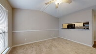 This well-appointed 1-bedroom, 1-bathroom residence offers a thoughtfully designed single-floor layout that maximizes both comfort and functionality. The living area immediately stands out with its vaulted ceiling accented by exposed beams and a ceiling fan, creating an airy, open atmosphere. Soft, neutral-toned carpet covers the living space floor, contributing to a warm and inviting ambiance. A distinctive pass-through window connects the living area to the kitchen, enhancing the sense of openness and allowing for easy interaction between spaces. The dining area features rich, dark wood-look flooring and is illuminated by a sleek pendant light, offering a seamless transition into the kitchen. The kitchen is outfitted with white cabinetry, dark granite-style countertops, a stainless steel sink, and black appliances including a refrigerator, range, and dishwasher. A window above the sink brings in natural light. The bathroom is clean and functional, showcasing the same dark wood-look flooring, a tub-shower combination with white tile surround, and dark countertop finishes that tie the space together cohesively. Neutral wall tones throughout the residence lend a versatile backdrop suited to a variety of interior styles.