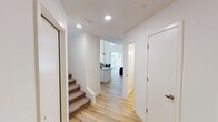 This thoughtfully designed three-story home blends contemporary style with functional living across a well-organized layout. Light-toned hardwood floors and crisp white walls flow throughout the main level, creating a clean, airy atmosphere. The open-concept kitchen is a standout feature, boasting white shaker cabinetry, a striking herringbone tile backsplash, stone-look countertops with an island ideal for bar seating, and a full suite of stainless steel appliances — all beneath soaring double-height ceilings. The adjoining dining area is anchored by a bold sputnik chandelier, adding a modern artistic touch. The living room opens directly to a private outdoor patio through sliding glass doors, inviting abundant natural light indoors. Bedrooms are outfitted with plush carpet, ceiling fans, and ample natural light; one features a walk-in closet for added convenience. A serene primary bathroom offers a dual-sink vanity, large mirrors, and a spacious walk-in glass shower adorned with herringbone tile. A dedicated laundry room houses a full-size washer and dryer with built-in shelving. The uppermost floor presents a versatile loft space with hardwood floors, a workspace, and a wall-mounted television — perfect as a home office or lounge.