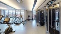 Located at 625 W Division Street in Chicago's vibrant Near North Side neighborhood, this well-appointed fitness center offers a comprehensive workout environment across a single, open floor. The space is thoughtfully divided into distinct training zones, each designed to support a variety of exercise routines.

The cardio area is positioned along a wall of floor-to-ceiling windows, flooding the space with natural light and offering views of the surrounding Chicago streetscape. A row of treadmills and stationary bikes with individual screen displays lines this bright perimeter, creating an engaging environment for endurance training.

Adjacent to the cardio zone, a functional training area features a durable dark rubber floor, TRX suspension trainers mounted to a textured accent wall, plyo boxes, a dumbbell rack, and a weight bench — providing ample options for bodyweight and free weight workouts. Full-length mirrors amplify the sense of space and allow for form monitoring during exercises.

The strength and cable machine section offers a variety of cable-based resistance equipment and multi-function machines, accommodating both isolated and compound movements. Recessed and cove lighting throughout the ceiling creates a clean, modern ambiance, while glass partitions and polished concrete-toned flooring contribute to the space's contemporary aesthetic. The overall design balances functionality with a sleek, professional atmosphere.
