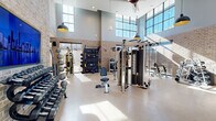 Located at 2501 N Orange Blossom Trail in Orlando, FL, this comprehensive fitness center spans a generously sized single floor, offering a well-appointed environment designed to support a full range of workout activities. The space is divided into two distinct zones, each thoughtfully designed to serve different fitness needs.

The main workout area is an architectural standout, featuring soaring double-height ceilings lined with expansive floor-to-ceiling windows that flood the space with natural light. Exposed brick walls lend an industrial yet inviting character, complemented by modern pendant lighting. This area is comprehensively equipped with a wide array of strength-training machines, cable systems, free weights, dumbbells, barbells, medicine balls, and functional training accessories, alongside a full lineup of cardio equipment including treadmills, ellipticals, stair climbers, and stationary bikes. Large wall mirrors enhance the sense of space throughout.

A separate group fitness studio is enclosed by sleek black-framed glass walls and doors, providing visual openness while maintaining acoustic separation. This room features wood-look flooring, floor-to-ceiling mirrors, a wall-mounted display screen for guided workouts, and dedicated sound speakers — ideal for yoga, Pilates, dance, or instructor-led classes. Together, the two areas form a well-rounded, modern fitness facility suited for diverse training styles.