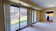This single-floor Dresden residence offers a thoughtfully arranged 3-bedroom, 2-bathroom layout designed for comfortable everyday living. The spacious living area is highlighted by warm neutral-toned walls, plush carpeting, and dual sliding glass doors that flood the space with natural light and provide direct access to an outdoor patio, framing views of a lush green lawn and mature trees. The open layout connects the living area seamlessly to the kitchen, which features rich dark wood cabinetry, granite-style countertops, wood-look flooring, and white GE appliances including a gas range and refrigerator. A window above the counter adds additional natural light to the kitchen area. Each of the three bedrooms is carpeted and painted in consistent warm tones, with large windows offering pleasant outdoor views of the surrounding greenery. The bedrooms provide ample wall space for furnishings and include standard closet storage. Both bathrooms are finished with wood-look flooring, white tiled tub-shower combinations, and granite-style countertops, maintaining a cohesive design throughout. The overall ambiance of the home is bright, clean, and functional, with a neutral palette that provides a versatile backdrop for a variety of interior styles.