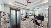 Located at 2841 Enterprise Rd in DeBary, Florida, this single-level fitness center is thoughtfully designed to support a full range of workout routines. The facility is divided into two distinct zones, each catering to different training styles.

The main cardio and strength area features a variety of Matrix-brand equipment, including treadmills, elliptical trainers, and a stationary bike. Full-length mirrored walls line one side of the room, visually expanding the space and allowing users to monitor their form. Textured, multi-tone carpet tiles cover the floor, providing comfort underfoot, while coffered ceilings with ceiling fans promote airflow throughout the room. Natural light filters in through multiple white-shuttered windows, creating a bright and inviting atmosphere. A dumbbell rack and additional strength machines round out the equipment offerings.

An adjacent functional training room offers a more open layout with smooth wood-look vinyl flooring, ideal for dynamic movement. This room is equipped with a cable machine, a plyo box, a medicine ball rack, and a wall-mounted mirror. Recessed lighting and a ceiling fan keep the space well-lit and comfortable. A glass-paned door separates this area from the main workout floor, providing flexibility for group or individual training sessions.