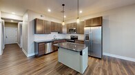 Located at 221 Trowbridge St, Unit 206 in Grand Rapids, Michigan, this well-appointed two-bedroom, two-bathroom unit offers a thoughtfully designed single-floor layout. The open-concept living, dining, and kitchen area serves as the heart of the home, featuring rich hardwood-style flooring, recessed lighting, and a seamless flow between spaces. The kitchen is a standout, boasting dark granite countertops, rich wood cabinetry, a white subway tile backsplash, a central island with pendant lighting, and a full suite of stainless steel appliances including a refrigerator with ice maker, range, microwave, and dishwasher. A long hallway connects the main living area to the private quarters, where both bedrooms are finished with plush carpeting and ample closet space. The primary bedroom includes a dedicated closet and direct access to a full bathroom. Both bathrooms are finished with stone-look tile flooring and dark wood vanities. One bathroom features a full tub-shower combo. Throughout the unit, neutral warm-toned walls, white trim, and black hardware accents provide a clean, modern aesthetic that is both functional and inviting.