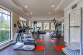 Located at 3400 Winterset Pkwy SE in Marietta, Georgia, this fitness center offers a thoughtfully designed workout facility built to support a full range of exercise routines. The space features a striking red-and-charcoal rubber tile floor, providing both durability and a bold aesthetic that energizes the room. Large windows line the walls on multiple sides, flooding the interior with natural light and offering pleasant views of the surrounding greenery, creating an inviting and motivating environment. Crown molding and recessed lighting add a polished, well-finished look to the crisp white walls and ceilings. A full wall of mirrors along one side visually expands the space and assists with form during workouts. The facility is equipped with a comprehensive selection of True-brand cardio machines, including treadmills, upright and recumbent stationary bikes, and a multi-function cable weight machine. A power tower for bodyweight exercises and a flat weight bench round out the strength training options. French doors with etched glass provide a welcoming entrance, while the open layout ensures ample room to move freely between stations. The overall ambiance is clean, bright, and functional, making this fitness center a well-appointed amenity for residents of the Winterset community.