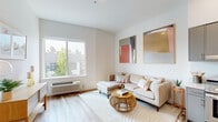 This thoughtfully designed single-floor residence offers a clean, contemporary aesthetic throughout, characterized by crisp white walls, light wood-style flooring, and an abundance of natural light. The open living area serves as the heart of the space, featuring a large sliding window that frames lush tree-lined views and allows sunlight to fill the room. The living space flows naturally toward the kitchen, which is outfitted with sleek gray cabinetry, light quartz countertops, stainless steel appliances including a range, refrigerator, dishwasher, and microwave, as well as open shelving for added functionality. A dedicated laundry area with in-unit washer is conveniently accessible just off the kitchen. The bedroom offers a serene retreat with plush carpeting, a generously sized sliding-door closet with a full hanging rod, and a bright window overlooking greenery. The overall ambiance is warm and inviting, with a neutral palette that lends itself to a variety of interior styles. Every area of the residence reflects a modern sensibility, combining practical storage solutions with an airy, well-lit atmosphere that makes the space feel comfortable and cohesive throughout.