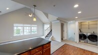 Located at Fairfield Broadway Knolls at Holbrook in Holbrook, NY, this two-floor residence offers a thoughtfully designed layout with a blend of comfort and functionality. The main level showcases a dramatic vaulted ceiling in the open-concept living and dining area, enhanced by recessed lighting and a ceiling fan. Natural light flows in through multiple windows, creating a bright and airy atmosphere. The kitchen is well-equipped with warm wood cabinetry, dark granite countertops, stainless steel appliances including a refrigerator, range, and microwave, and durable hardwood-style flooring. A kitchen island with matching cabinetry provides additional prep and storage space. A dedicated laundry area with side-by-side washer and dryer units, as well as a half bath featuring accessibility grab bars and tile flooring, round out the main level. The carpeted staircase leads to the upper floor, where a generously sized bedroom with crown molding, a ceiling fan, and plush carpet offers a comfortable retreat, complete with access to a walk-in closet. An additional versatile carpeted room with recessed lighting provides flexible living space. The full bathroom upstairs features a tub and shower combination with sliding glass doors and chrome fixtures, finished with clean tile work and crown molding accents.