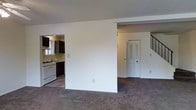This two-floor residence offers a practical and well-organized layout designed for comfortable everyday living. The main level features an open-concept design that seamlessly connects the living area to the kitchen, creating a cohesive and functional space. The living area is finished with plush carpeting that extends throughout, adding warmth and comfort underfoot.

The kitchen is equipped with dark cabinetry that provides ample storage, a gas range with a white finish, and a sink positioned beneath a window that allows natural light to filter in. The contrast between the dark cabinets and light countertops and walls gives the kitchen a clean, defined aesthetic.

A partial dividing wall separates the living space from the entryway area, where a closet with louvered doors offers convenient storage. A staircase leads to the upper floor, rounding out the main level's layout. The walls throughout are finished in crisp white, contributing to a bright and neutral atmosphere that is easy to personalize. Overall, the space presents a straightforward and livable design with a clear separation of functional zones across both floors.