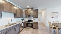 This thoughtfully designed 2-bedroom, 2-bathroom single-floor residence makes efficient use of its space with a clean, modern aesthetic throughout. Light-toned luxury vinyl plank flooring flows seamlessly across the main living areas, complementing the bright white walls and creating an airy, cohesive feel.

The kitchen is a standout feature, equipped with rich dark-brown shaker-style cabinetry, granite-look countertops, a white subway tile backsplash, and a full suite of stainless steel appliances including a range, over-the-range microwave, dishwasher, and refrigerator. The kitchen opens directly to the dining area, which comfortably accommodates a full dining set and offers a natural transition to the living room.

The living room is bright and welcoming, with clean walls and light flooring. The primary bedroom is generously sized, featuring a walk-in closet with wire shelving for ample storage. The second bedroom is carpeted and receives natural light through a window with neighborhood views. Both bathrooms mirror the kitchen's design language, featuring granite-look vanity countertops and dark cabinetry.

A dedicated laundry room houses a full-size washer and dryer with overhead wire shelving, adding everyday convenience. A hallway closet provides additional storage, completing this well-organized and move-in-ready residence.