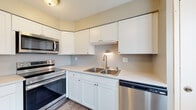 This two-story home offers a thoughtfully designed layout across two levels, connected by a carpeted staircase with a classic white-painted banister. The main level features an open living area with neutral-toned carpet, providing a clean and versatile space for everyday living. The kitchen is equipped with a full suite of stainless steel appliances, including a refrigerator, electric range, over-the-range microwave, and dishwasher. White shaker-style cabinetry with brushed nickel hardware lines the walls, complemented by light countertops and wood-look flooring that adds warmth to the space. A double-basin stainless steel sink with a modern faucet is centrally positioned beneath the upper cabinets. Upstairs, the bedrooms are finished with plush carpet and neutral wall tones, offering comfortable and functional spaces. At least one bedroom features a walk-in closet with built-in shelving. The bathrooms are well-appointed, with one featuring a marble-look countertop with an undermount sink and framed mirror, while another includes a warm wood-toned vanity with a dual-sink white countertop and brushed nickel fixtures. Throughout the home, consistent neutral tones and clean finishes create a cohesive and move-in-ready ambiance.