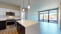 Located at 1632 N Franklin Pl in Milwaukee's vibrant 53202 zip code, this contemporary single-floor residence showcases a thoughtfully designed open-concept layout with modern finishes throughout. The kitchen is a standout centerpiece, featuring a large quartz-topped island with dark cabinetry and matte black hardware, complemented by crisp white upper cabinets, a classic subway tile backsplash, and a full suite of stainless steel appliances. Pendant lighting adds warmth and visual interest above the island. The kitchen flows seamlessly into the open living area, which is bathed in natural light and provides direct access to a private balcony through expansive floor-to-ceiling sliding glass doors. The bedrooms are carpeted for comfort and feature large black-framed windows that frame neighborhood views and invite abundant daylight. A walk-in closet with a built-in wire shelving system offers generous, well-organized storage. The bathrooms are finished with large-format tile flooring, dark wood vanities topped with white counters, and backlit mirrors, delivering a clean and modern aesthetic. The space is unified by light wood-tone flooring throughout the main living areas, neutral wall tones, and a cohesive contemporary design palette.
