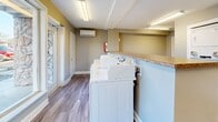 Located at 203 Sealey Drive in Madison, Tennessee, this shared laundry facility offers a clean, efficiently organized space designed for convenient communal use. The single-floor layout makes practical use of its footprint, accommodating a row of Speed Queen commercial top-load washing machines along one side, complemented by a laminate countertop surface ideal for folding and sorting laundry. Along the back wall, a bank of stacked dryer units provides ample drying capacity for multiple users. The room is finished with durable wood-look vinyl plank flooring throughout, providing easy maintenance and a tidy aesthetic. Neutral-toned walls contribute to a clean, utilitarian atmosphere, while fluorescent lighting ensures the space is well-lit. A wall-mounted mini-split HVAC unit provides climate control for year-round comfort. Natural light filters in through windows along one wall, adding a welcoming brightness to the room. Additional utility is provided by two closet doors, likely housing storage or mechanical equipment. An electrical panel and posted service information are also accessible on the wall. The facility is managed through CSC ServiceWorks, offering users a straightforward and reliable laundry experience.