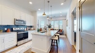 Located at 1040 Enclave Piney Lane in Asheville, NC, this thoughtfully designed single-floor home offers a seamless open-concept layout filled with natural light and modern finishes throughout. The gourmet kitchen is a standout centerpiece, showcasing white shaker cabinetry, granite countertops, a large island with bar seating, stainless steel appliances, and a striking blue tile backsplash. Elegant brass pendant lights hang above the island, adding warmth and style. The kitchen flows effortlessly into the dining area and living room, where large windows with plantation blinds invite abundant natural light and outdoor views. The dining space features soaring ceilings and additional windows that further enhance the airy atmosphere. Hardwood flooring runs throughout the main living areas, adding continuity and warmth. The bedrooms are carpeted and generously sized, each offering multiple windows and ample closet space, including a spacious walk-in closet. The primary bathroom is well-appointed with granite countertops, white cabinetry, and hardwood-style flooring. This home combines clean architectural lines with upscale finishes, creating a bright, welcoming, and functional living environment in the heart of Asheville.