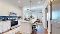 Located at 1040 Enclave Piney Lane in Asheville, NC, this thoughtfully designed single-floor home offers a seamless open-concept layout filled with natural light and modern finishes throughout. The gourmet kitchen is a standout centerpiece, showcasing white shaker cabinetry, granite countertops, a large island with bar seating, stainless steel appliances, and a striking blue tile backsplash. Elegant brass pendant lights hang above the island, adding warmth and style. The kitchen flows effortlessly into the dining area and living room, where large windows with plantation blinds invite abundant natural light and outdoor views. The dining space features soaring ceilings and additional windows that further enhance the airy atmosphere. Hardwood flooring runs throughout the main living areas, adding continuity and warmth. The bedrooms are carpeted and generously sized, each offering multiple windows and ample closet space, including a spacious walk-in closet. The primary bathroom is well-appointed with granite countertops, white cabinetry, and hardwood-style flooring. This home combines clean architectural lines with upscale finishes, creating a bright, welcoming, and functional living environment in the heart of Asheville.