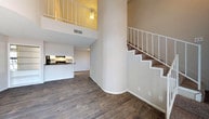 Located at 7600 Blanco Rd in San Antonio, Texas, this two-story residence offers a striking open layout defined by soaring vaulted ceilings that lend a dramatic sense of height and spaciousness to the main living area. Dark hardwood-style flooring runs throughout both levels, providing a warm, cohesive aesthetic. A white-railed staircase with carpeted treads connects the floors, with the upper level featuring a loft-style overlook that adds architectural interest and an open, airy feel.

The kitchen is efficiently laid out in a galley style, featuring white cabinetry, dark countertops, a skylight overhead, and black appliances including a refrigerator and range. A pass-through counter connects the kitchen to the main living space, making the layout practical and sociable.

The upper level includes a well-proportioned bedroom with vaulted ceilings, a ceiling fan, and a window that allows natural light to filter in. Closet space is provided by a walk-in closet with built-in shelving. The bathrooms are clean and functional, with one featuring a tub-shower combination and wood-look tile flooring, and another with a dark-topped vanity and textured walls. Neutral tones and clean finishes throughout create a calm, move-in-ready atmosphere.