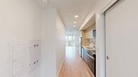 Located at 4508 California Ave SW in Seattle's vibrant West Seattle neighborhood, this thoughtfully designed unit offers a clean, contemporary aesthetic throughout. Light-toned hardwood flooring runs continuously across the entire single-floor layout, lending warmth and visual cohesion to every room.

The open living areas are bathed in natural light thanks to large floor-to-ceiling windows and a sliding glass door that opens onto a private balcony, offering elevated views of the surrounding Seattle cityscape. Recessed ceiling lighting throughout adds to the bright, airy atmosphere.

The galley-style kitchen is efficiently arranged along one wall, featuring light wood cabinetry, stainless steel appliances including a refrigerator and dishwasher, a built-in cooktop, and a sleek undermount sink — all designed to maximize functionality within a compact footprint.

The bathroom is finished with the same modern sensibility, showcasing a light wood vanity with a white countertop, an undermount sink, a large mirror with integrated lighting, and clean white walls. A dedicated closet provides practical storage solutions.

The overall design emphasizes minimalism and functionality, with crisp white walls, clean lines, and thoughtful use of space creating a calm and livable environment well-suited to urban living in Seattle.