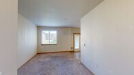 Located in Yelm, WA, this single-floor unit offers a clean, functional layout designed for comfortable everyday living. The living area is finished with soft carpeting and neutral-toned walls, creating a bright and welcoming atmosphere. A large window frames views of the surrounding grounds and neighboring buildings, allowing natural light to fill the space. A door provides convenient access to the exterior.

The kitchen is a standout feature, outfitted with rich dark cabinetry, granite-style countertops, and wood-look flooring that adds warmth and contrast. Black appliances, including a full-size refrigerator and range, are complemented by a double basin sink and track lighting overhead, making it both stylish and practical.

The bedroom areas continue the carpeted flooring theme, with one room featuring dual windows fitted with blinds that invite natural light while offering privacy. A sliding door closet provides organized storage space with a full-width hanging rod. The rooms are finished with warm wood trim along the baseboards, tying together the overall aesthetic.

The unit's neutral color palette and open feel make it a versatile and move-in ready space, well-suited for a variety of living arrangements in the Yelm community.