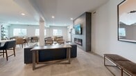 Located at 2220 Majoros Rd in West Kelowna, BC, this well-appointed communal amenity space offers a thoughtfully designed, open-concept layout across a single floor. Large-format tile flooring flows seamlessly throughout, unifying the kitchen, dining, and living areas into a cohesive and inviting environment.

The kitchen is outfitted with stainless steel appliances, white cabinetry, a classic subway tile backsplash, open shelving, and a central island with seating for several guests. Pendant lighting adds a modern touch above the island counter.

The dining area accommodates multiple seating arrangements, with several tables and upholstered chairs positioned to encourage social interaction. Natural light enters through generously sized windows, while curated artwork—including a striking large-scale abstract painting—adds visual interest to the crisp white walls.

The living area serves as a focal point of the space, anchored by a floor-to-ceiling dark tile feature wall housing a linear electric fireplace and a wall-mounted television. A richly textured live-edge coffee table and a deep blue leather sofa contribute warmth and character to the contemporary setting.

A smaller nook near the entrance provides an intimate dining spot with additional natural light and a mini-split climate control unit, offering flexibility and comfort for residents year-round.
