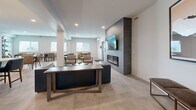Located at 2220 Majoros Rd in West Kelowna, BC, this well-appointed communal amenity space offers a thoughtfully designed, open-concept layout across a single floor. Large-format tile flooring flows seamlessly throughout, unifying the kitchen, dining, and living areas into a cohesive and inviting environment.

The kitchen is outfitted with stainless steel appliances, white cabinetry, a classic subway tile backsplash, open shelving, and a central island with seating for several guests. Pendant lighting adds a modern touch above the island counter.

The dining area accommodates multiple seating arrangements, with several tables and upholstered chairs positioned to encourage social interaction. Natural light enters through generously sized windows, while curated artwork—including a striking large-scale abstract painting—adds visual interest to the crisp white walls.

The living area serves as a focal point of the space, anchored by a floor-to-ceiling dark tile feature wall housing a linear electric fireplace and a wall-mounted television. A richly textured live-edge coffee table and a deep blue leather sofa contribute warmth and character to the contemporary setting.

A smaller nook near the entrance provides an intimate dining spot with additional natural light and a mini-split climate control unit, offering flexibility and comfort for residents year-round.