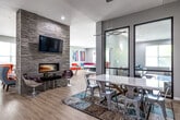 Located at 3306 Lincoln Way in Ames, Iowa, this single-floor community space offers a generously sized, thoughtfully designed amenity area built for both socializing and productivity. The open floor plan flows naturally between distinct zones, all finished with light wood-style flooring that unifies the layout and enhances brightness throughout.

The centerpiece of the main gathering area is a dramatic floor-to-ceiling stacked stone accent wall, home to a sleek linear fireplace and a wall-mounted flat-screen TV. Modern swivel chairs and lounge seating are arranged around the fireplace, creating an inviting focal point. Adjacent to this is a stylish dining area featuring a white table paired with mixed metal and modern chairs, illuminated by a contemporary pendant light fixture.

The living room area offers comfortable neutral sofas and armchairs accented with blue and patterned pillows, anchored by a bold blue abstract area rug. Black-framed glass partition doors add an architectural element while maintaining visual connectivity between spaces.

A dedicated conference room provides a focused work environment, equipped with a white meeting table, rolling chairs, a wall-mounted TV, and a whiteboard. A spacious game room with large windows allowing abundant natural light accommodates a ping pong table and foosball table. Colorful contemporary artwork is displayed throughout, contributing to the vibrant and energetic ambiance of the overall space.
