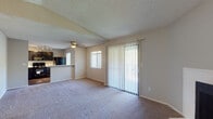 This single-floor residence offers a comfortable and functional layout designed for everyday living. The open living and dining area is carpeted throughout and bathed in natural light from multiple windows fitted with blinds and a sliding glass door that opens to an outdoor balcony or patio. A classic white fireplace serves as a focal point in the living room, adding warmth and character to the space. A ceiling fan overhead completes the room's practical comfort features. The textured ceilings are consistent throughout the home.

The kitchen is equipped with dark cabinetry, white countertops, and a white subway tile backsplash. Black appliances — including a refrigerator, electric range, built-in microwave, and double-basin sink — provide a cohesive, modern contrast to the light countertops. Wood-look flooring grounds the kitchen's design.

The bedrooms are carpeted and well-sized, each offering sliding closet doors for convenient storage. The primary bathroom features dark cabinetry with a white countertop, a large mirror with overhead lighting, and a tub-shower combination. A secondary bathroom includes a glass-enclosed shower stall, toilet, and towel bar, finished with wood-look flooring. Throughout, the neutral color palette creates a clean, move-in ready atmosphere.