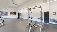 This well-equipped fitness center at 1 Catawba Cir in Columbia, SC, offers a spacious, single-floor layout designed to support a comprehensive workout experience. The room features soaring vaulted ceilings that lend an open, airy feel, complemented by sleek linear LED lighting running the length of the space. Ceiling fans provide additional airflow and comfort throughout the room.

A full wall of large, floor-to-ceiling windows lines one side of the facility, flooding the interior with natural light and offering direct views of the outdoor pool and surrounding landscaping — a motivating backdrop for any workout. The durable speckled rubber flooring is both practical and visually clean, providing excellent traction and cushioning underfoot.

The cardio zone is well-stocked with a row of True-brand treadmills, elliptical trainers, and stair climbers, all positioned to take advantage of the pool-facing views. The strength training area features a multi-function cable machine, a power rack with bench press, and a free weights section complete with barbells, weight plates, and a rack of stability balls. Motivational athletic photography adorns the walls, enhancing the energetic atmosphere. This fitness center is comprehensively outfitted to serve a wide range of workout preferences in a bright, well-designed environment.