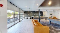 Located at 6854 Governors West NW, this expansive single-floor amenity space offers a thoughtfully designed environment for recreation, work, and socializing. The open-concept game lounge serves as a centerpiece, featuring a pool table, ping-pong table, and a bold dark accent wall with geometric paneling, anchored by a large leather sofa and area rug. Industrial-style exposed ductwork and a dark ceiling complement the modern aesthetic, while large windows and glass-panel garage doors flood the space with natural light and provide seamless indoor-outdoor connectivity.

The kitchen and common area boasts striking chevron-patterned hardwood flooring, rich wood ceiling beams, quartz countertops, dark cabinetry, and a utility sink — ideal for hosting and gatherings. The hallway connects zones with ease, featuring light tile flooring, exposed cylindrical ductwork, warm leather accent chairs, and curated wall art, creating an inviting transitional space.

The dedicated office area includes individual built-in workstations with white surfaces, stylish decorative mirrors, and warm accent lighting, offering a focused and attractive environment for remote work. A bathroom rounds out the functional offerings. Throughout the space, a cohesive blend of modern industrial design, warm textures, and contemporary furnishings creates an engaging and versatile community destination.