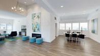 This contemporary single-floor residence showcases a thoughtfully designed open-concept layout that seamlessly connects the kitchen, dining, and living areas. The kitchen is a standout feature, equipped with dark espresso cabinetry, a white quartz waterfall island with bar seating, subway tile backsplash, stainless steel appliances, and a trio of globe pendant lights that add warmth and elegance overhead. Wood-look tile flooring runs throughout, lending warmth and cohesion to the entire space. The expansive living area centers around a sleek, floor-to-ceiling textured accent wall housing a modern linear fireplace, creating a striking focal point. Colorful abstract artwork and teal accent furnishings inject personality and vibrancy into the otherwise clean, neutral palette. The dining area benefits from generous natural light streaming through large windows, complemented by recessed lighting throughout for a bright, airy ambiance. The overall design aesthetic is clean and modern, with high ceilings amplifying the sense of space and openness. Every detail, from the minimalist furniture to the carefully chosen décor, reflects a refined, contemporary sensibility that makes this residence both visually impressive and highly functional.
