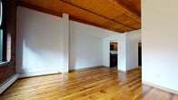 Located at 45 Willow St in Springfield, Massachusetts, this single-floor unit showcases a distinctive industrial character with a thoughtful blend of raw and refined finishes throughout. The open living area immediately impresses with warm hardwood floors, soaring wood-planked ceilings supported by exposed timber beams, and track lighting running along the ceiling. Large windows along the exposed brick walls allow natural light to fill the space, highlighting the rich texture of the original masonry.

The kitchen is well-appointed with warm wood cabinetry, dark countertops, a stainless steel sink, and black appliances including a range, dishwasher, and overhead microwave. Stone-look tile flooring grounds the kitchen with a durable, practical surface that complements the overall aesthetic.

The bedroom is generously proportioned, featuring plush carpet flooring, dramatic ceiling height with the same wood-beam ceiling detail, and prominent exposed brick walls with arched window openings that lend architectural charm and bring in natural light.

The bathroom is cleanly finished with a wood-framed vanity, stone-look tile flooring, and a full tub-shower combination with white subway tile surround. Throughout the space, the interplay of exposed brick, natural wood, and neutral walls creates a cohesive, loft-inspired ambiance.