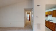 This single-floor residence offers a well-organized layout with a variety of architectural details that add character throughout. The main living area is a standout space, featuring soaring vaulted ceilings, a skylight that draws in natural light, a ceiling fan, and wainscoting along the walls, creating an open and airy atmosphere. A pendant light fixture adds a decorative touch overhead.

The hallway connects the living spaces efficiently, lined with wainscoting consistent with the rest of the unit, and includes climate control features such as a wall thermostat and ventilation registers. The carpeted bedrooms are comfortably sized, each benefiting from windows fitted with blinds that allow natural light while maintaining privacy. Textured ceilings are present in the bedroom areas.

The kitchen is equipped with warm oak cabinetry, white appliances including a coil-top electric range and a full-size refrigerator, a double-basin stainless steel sink with white countertops, and tile flooring, providing a practical and functional workspace.

The bathroom features a wood-toned vanity with ample under-sink storage, a wide mirror illuminated by a full-width vanity light bar, and a full tub and shower combination with chrome fixtures, complemented by tile flooring throughout.